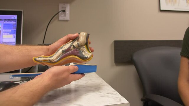 Foot care doctor with client showing custom shoe sole inserts on skeleton.