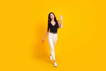 Fototapeta na wymiar Full size photo of young attractive girl happy positive smile go walk wave hand hello hi isolated over yellow color background