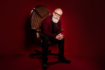 Full size portrait of minded person sit in leather chair look attentivey camera isolated on maroon...