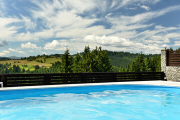 The pool overlooks the green mountains overgrown with fir trees on a sunny day.
