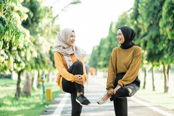 Obraz premium two girls in veil stretching their leg muscles by lifting and holding the bent leg with their arms before jogging in the park