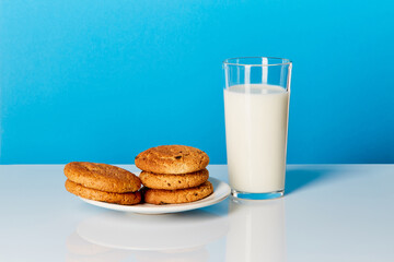 A glass of milk and cookies on a wooden table on a blue background.
