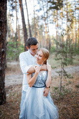 Happy young couple on a walk in the forest at sunset. The bride is wearing a blue wedding dress.