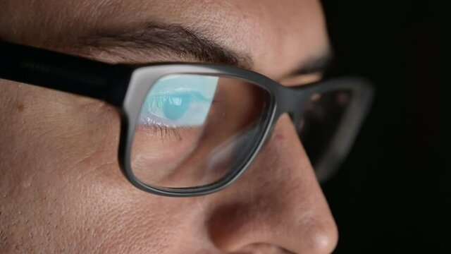 Close up portrait of a software engineer who is working: the eyes are focused on the screen where he is processing the instructions of the program. On the lens of the glasses we see their reflection.