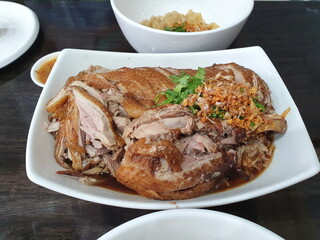Delicious Stewed Duck topped with sauteed garlic and coriander served in a white plate on a wooden table. It's a very popular menu item, paired with noodles, steamed rice, and a mellow sauce
