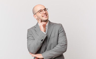 bald businessman smiling happily and daydreaming or doubting, looking to the side