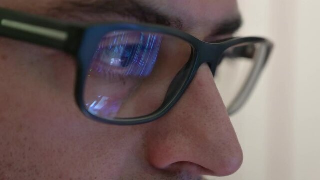 Close up portrait of a software engineer who is working: the eyes are focused on the screen where he is processing the instructions of the program. On the lens of the glasses we see their reflection.