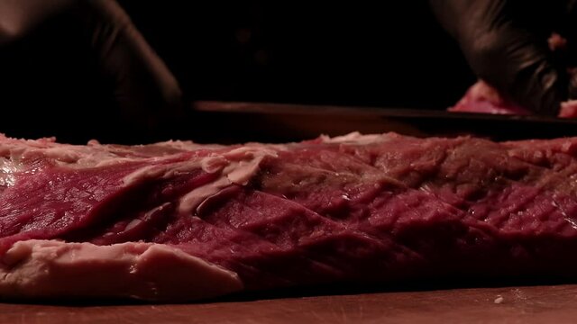 Chef is cutting raw beef tenderloin on a wooden board. Marbled meat. Dark atmosphere. Close up