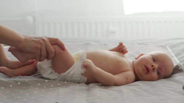 Mother with baby boy doing exercise simple exercises to make baby bones and muscles stronger, newborn infant lying on bed against the window. High quality 4k footage
