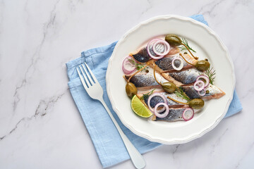 Salted herring with spice, herbs and onion on white plate on light stone background with copy space. Marinated sliced fish. Food with healthy unsaturated fats, flat lay
