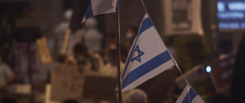 Israeli flags waving during protests against the government at night. Slow motion.