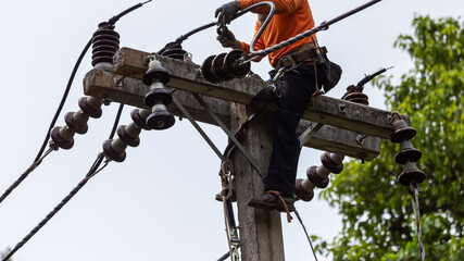 Rural electric poles are being repaired by electricians installing wires to connect. The tops of...