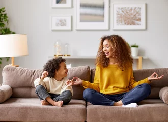 Ingelijste posters Happy afro american family mother and son in lotus pose meditating together in living room at home © JenkoAtaman