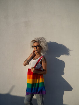Mujer joven con tatuajes sujetando un bolso con la bandera del orgullo gay 