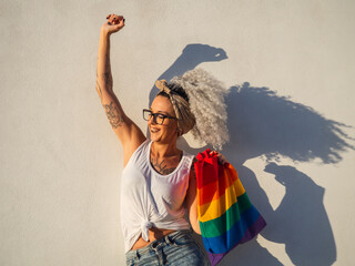 Mujer joven con tatuajes sujetando un bolso con la bandera del orgullo gay 