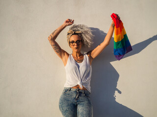 Mujer joven con tatuajes sujetando un bolso con la bandera del orgullo gay 