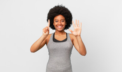 black afro woman smiling and looking friendly, showing number six or sixth with hand forward,...