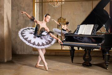 Young ballerina in a white tutu dancing on beautiful old piano in a vintage interior