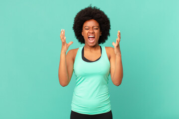 black afro woman furiously screaming, feeling stressed and annoyed with hands up in the air saying...