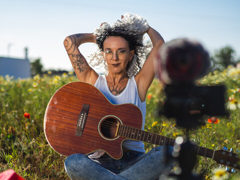 Mujer joven con tatuajes grabando un videoblog con la guitarra