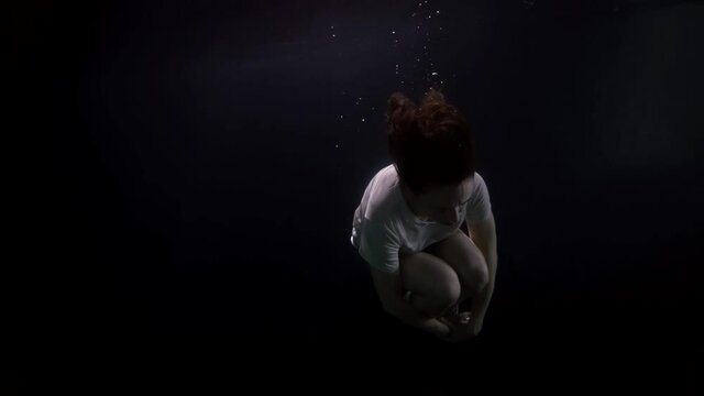 adult woman in fetal position is floating underwater, female figure in darkness of deepness