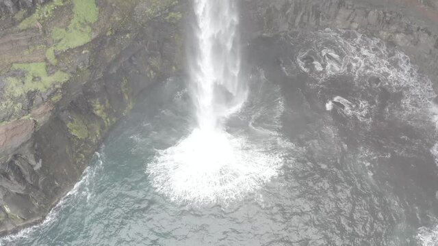 Mulafossur Waterfall dropping into the ocean on a cloudy and rainy day on Vagar Island in the Faroe Islands.