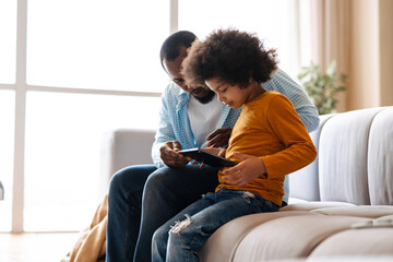 Black father and son using tablet computer while sitting on sofa at home