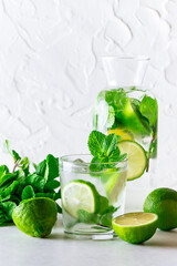 Healthy detox iced drink in a glass with lime and mint on white concrete background. Healthy lifestyle concept. Summer cold cocktail.