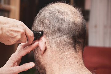 Wife cutting husbands hair at home with a haircut machine or hair clipper.
