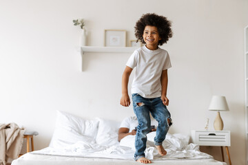 Black boy making fun on bed while his father using tablet computer