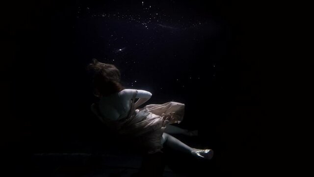 female figure in darkness depth of ocean or sea, underwater shot, woman is floating