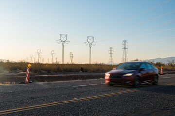 Electric pylons at sunset. Cars drive by on street. 