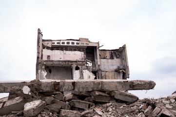 Fototapeta na wymiar A destroyed building against a gray sky with a pile of concrete rubble in the foreground. Background