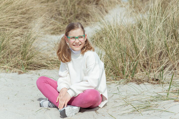 Portrait of pretty little girl sitting on white sand in dunes on Baltic sea