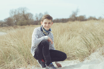 Portrait of handsome teenage boy sitting and smiling on white sand on Baltic sea beach