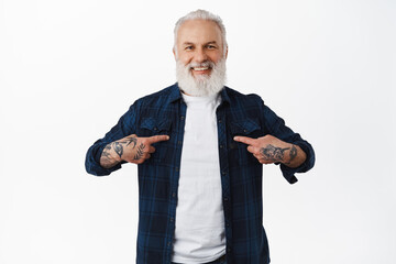 Smiling old stylish guy with tattoos and beard, pointing at himself, choose me, wants to volunteer,...