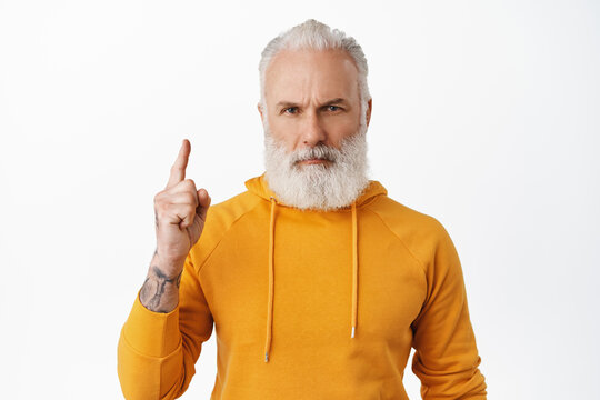 Serious Hipster Old Man Frowning, Pointing Finger Up At Something Important, Read Caption, Showing Link Or Advertisement Above, Standing Over White Background