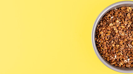 Organic homemade roasted granola cereal with oats, flax, almonds, chocolate in round baking tray on bright yellow background. Top view, flat lay muesli wide banner with copy space