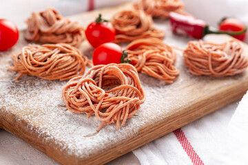 Homemade spaghetti with pepper and tomato flavor on wooden board on a light concrete background, top view