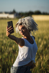 Chica delgada guapa con pelo muy rizado tomandose fotos en un campo de trigo al atardecer