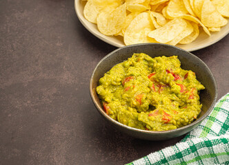 Fresh guacamole on a dish on a wooden cutting board and potato chips on a plate.  Avocado food recipe. Side view with copy space for text. Concept of healthy fruit and traditional Mexican foods