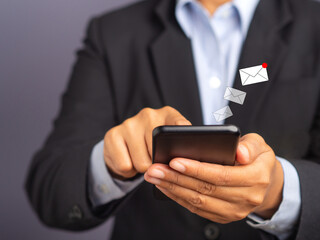 Businessman using a smartphone with an email icon while standing with a gray background. Space for text. Communication and technology concept