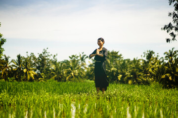 artistic portrait of young attractive and happy Asian woman outdoors at green rice field landscape dancing and doing spiritual meditation on beautiful nature background 