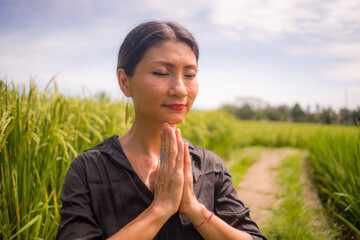 artistic portrait of young attractive and happy Asian woman outdoors at green rice field landscape dancing and doing yoga relaxation exercise and meditation  
