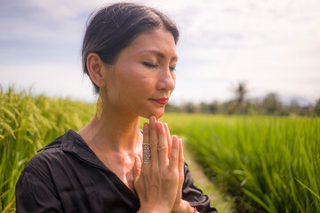 artistic portrait of young attractive and happy Asian woman outdoors at green rice field landscape dancing and doing yoga relaxation exercise and meditation  
