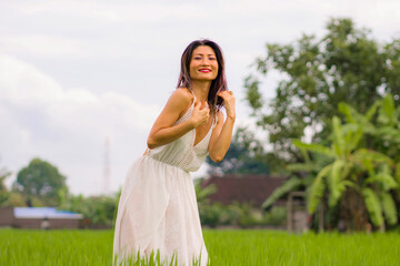 Fototapeta na wymiar artistic portrait of young attractive and happy Asian woman outdoors at green rice field landscape wearing elegant long dress dancing on beautiful nature carefree 