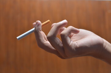 the gesture of a male hand holding a cigarette against a wooden background