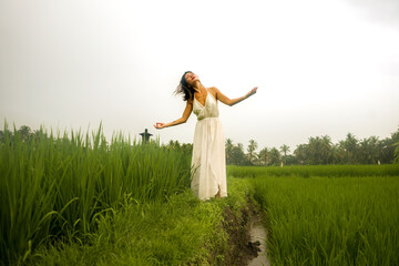 Naklejka na ściany i meble artistic portrait of young attractive and happy Asian woman outdoors at green rice field landscape wearing elegant long dress dancing on beautiful nature carefree 