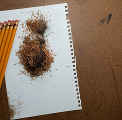 eraser capped wooden pencils with pencil sharpener shavings on a blank piece of paper, all on a...