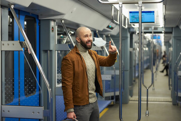 Fototapeta na wymiar A man with a beard is taking off a medical face mask and smiling on a train.